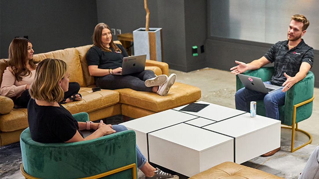 Four people seated on couches and chairs talking together.